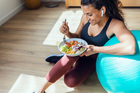 Woman enjoying healthy food while leaning on exercise ball. 