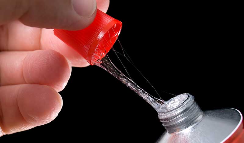 A hand opening a tube of glue. There is a thread of adhesive between the cap and the tube.
