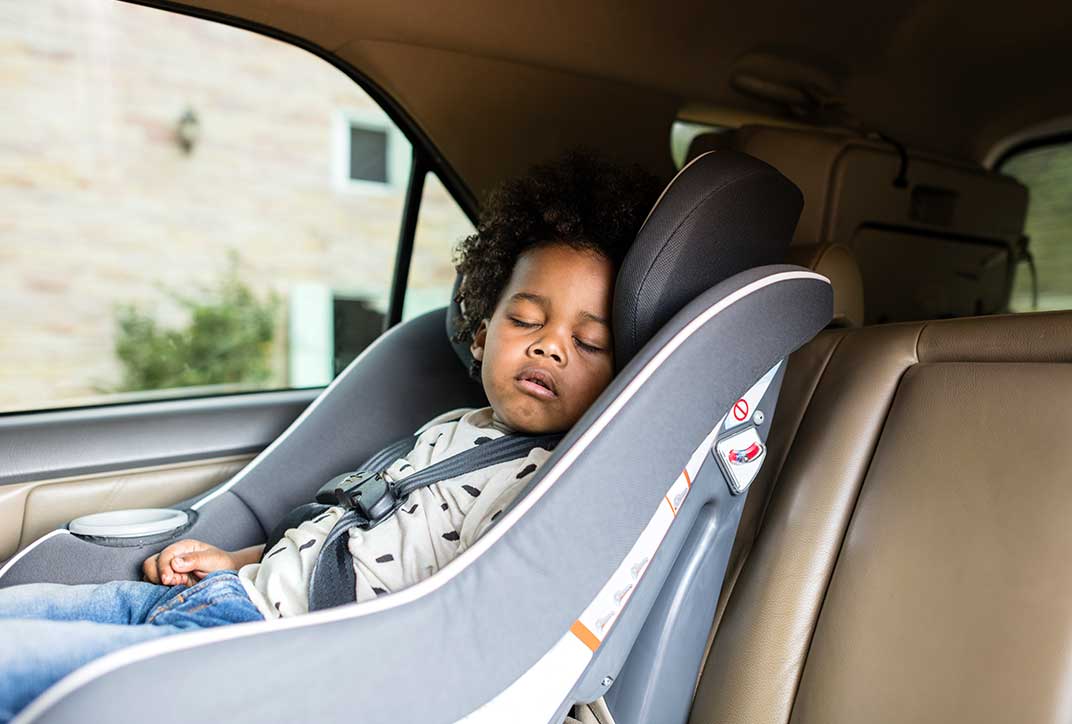 Ein Kleinkind sitzt schlafend im Kindersitz eines Autos.