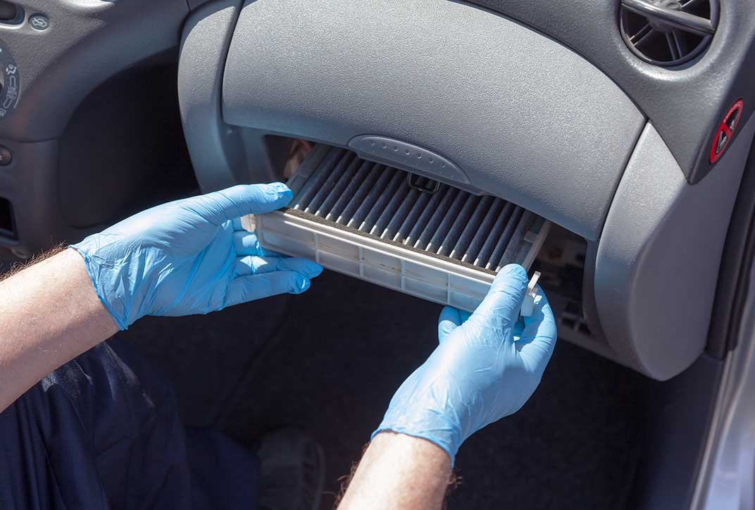 A person wearing protective gloves replacing the filter in a car ventilation system.