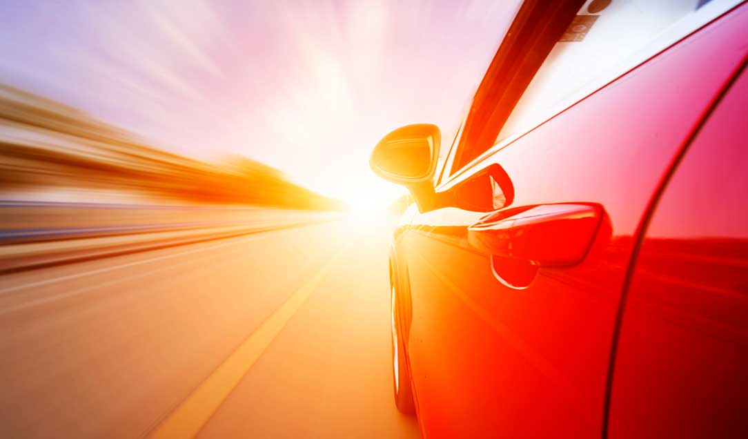 A car in motion. The side of the car is visible. In the background, the sun is setting.