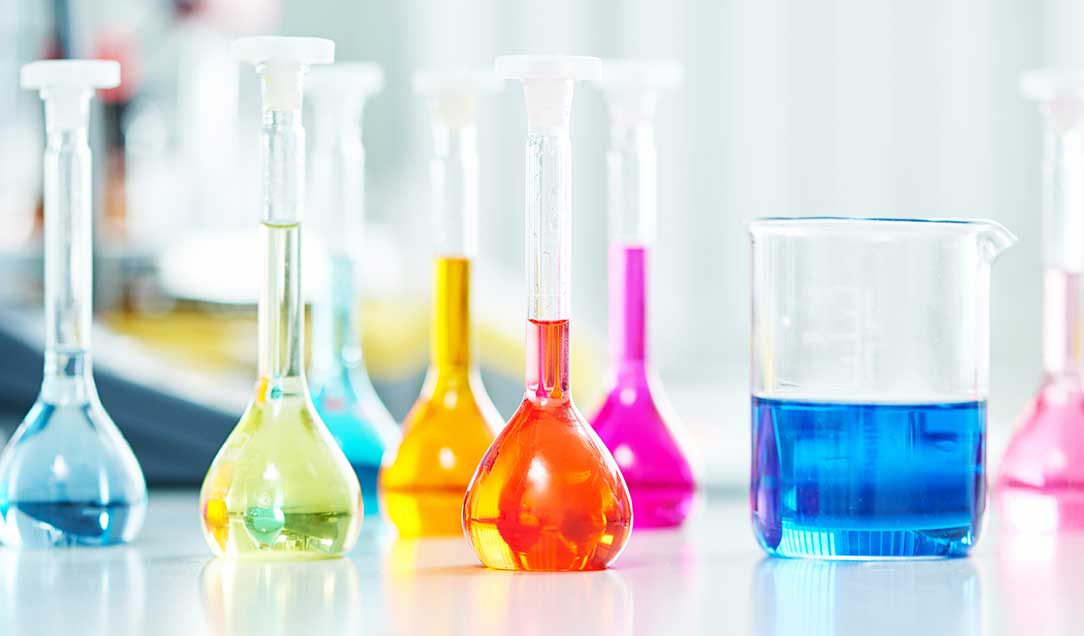 Verschiedene gläserne Stehkolben aus dem Chemielabor, die mit bunten Flüssigkeiten gefüllt sind.