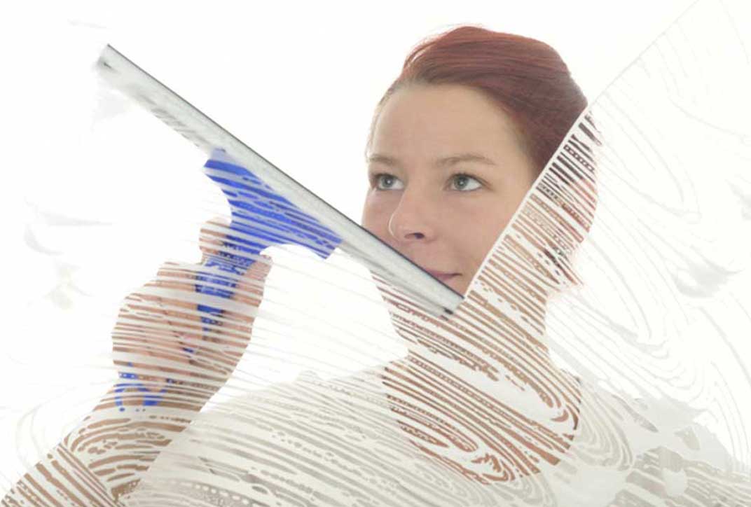 A young woman stands behind a soaped glass pane and starts to wipe it with a squeegee.
