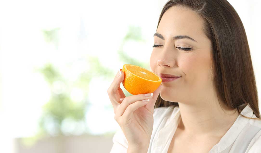 A lady with her eyes closed is inhaling the scent of half an orange.