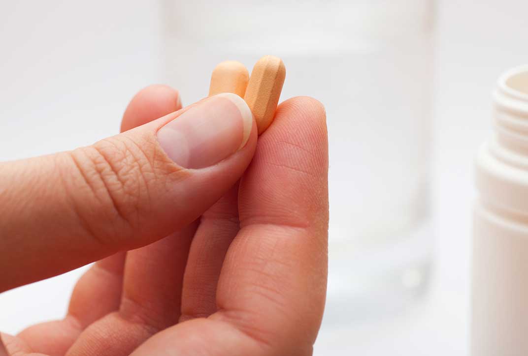 Eine Hand hält zwei orangefarbene Tabletten.
