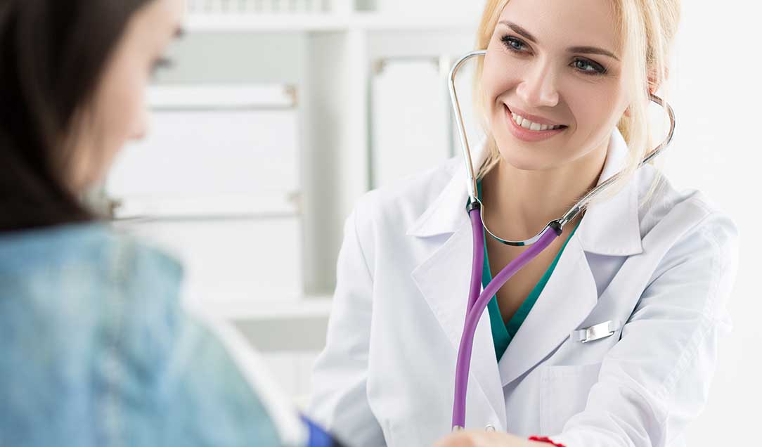 Eine Ärztin in einem weißen Kittel misst den Blutdruck einer Patientin.