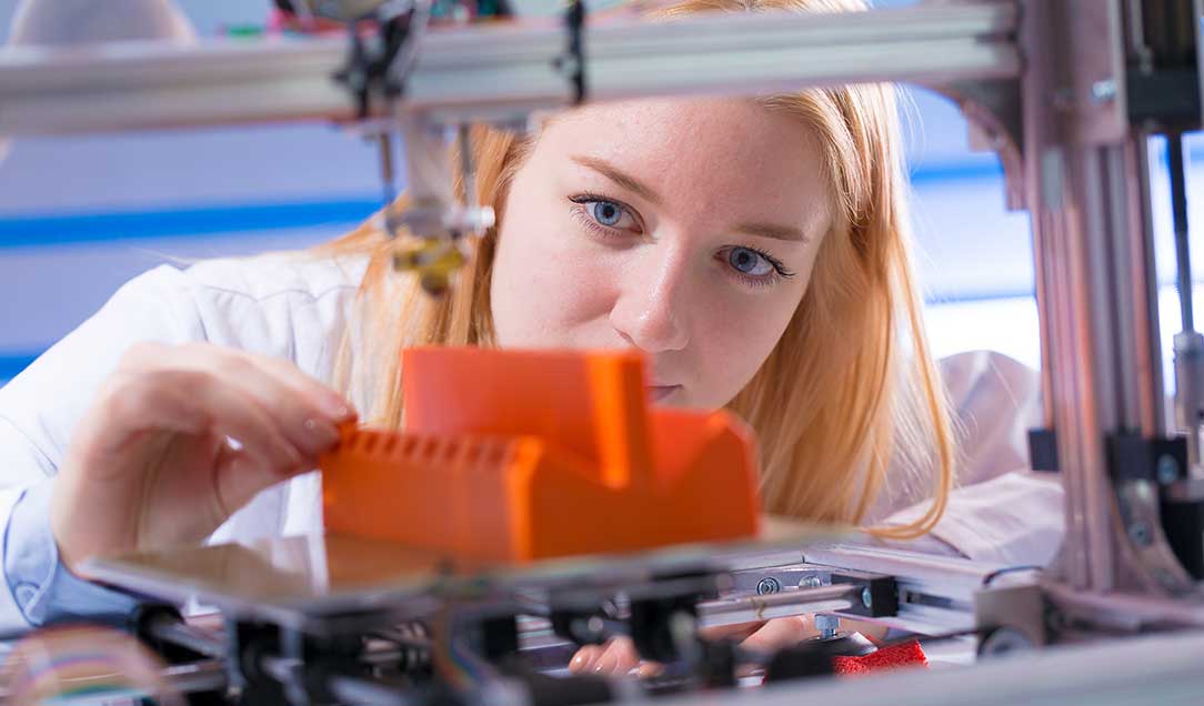 A woman is inspecting the output of a 3D printer.