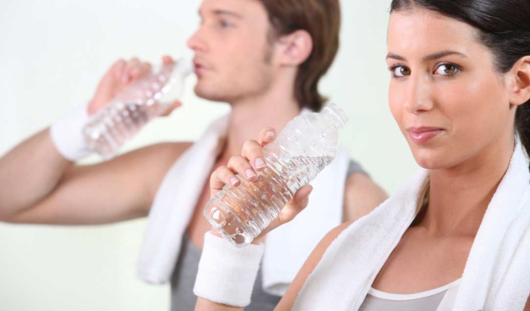 A woman and a man in the background. Both have a white towel over their shoulders and hold a plastic water bottle in their hands.