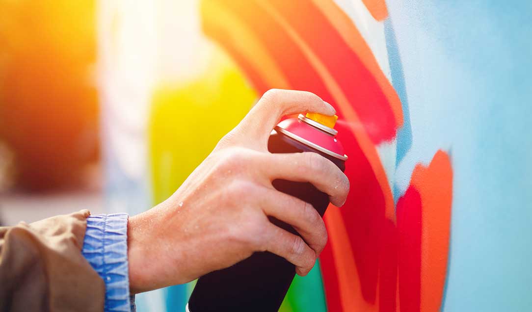 A hand with a spray can sprays a colorful graffiti on a wall.