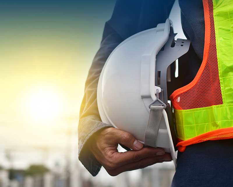 Worker with safety vest holding helmet under him arm